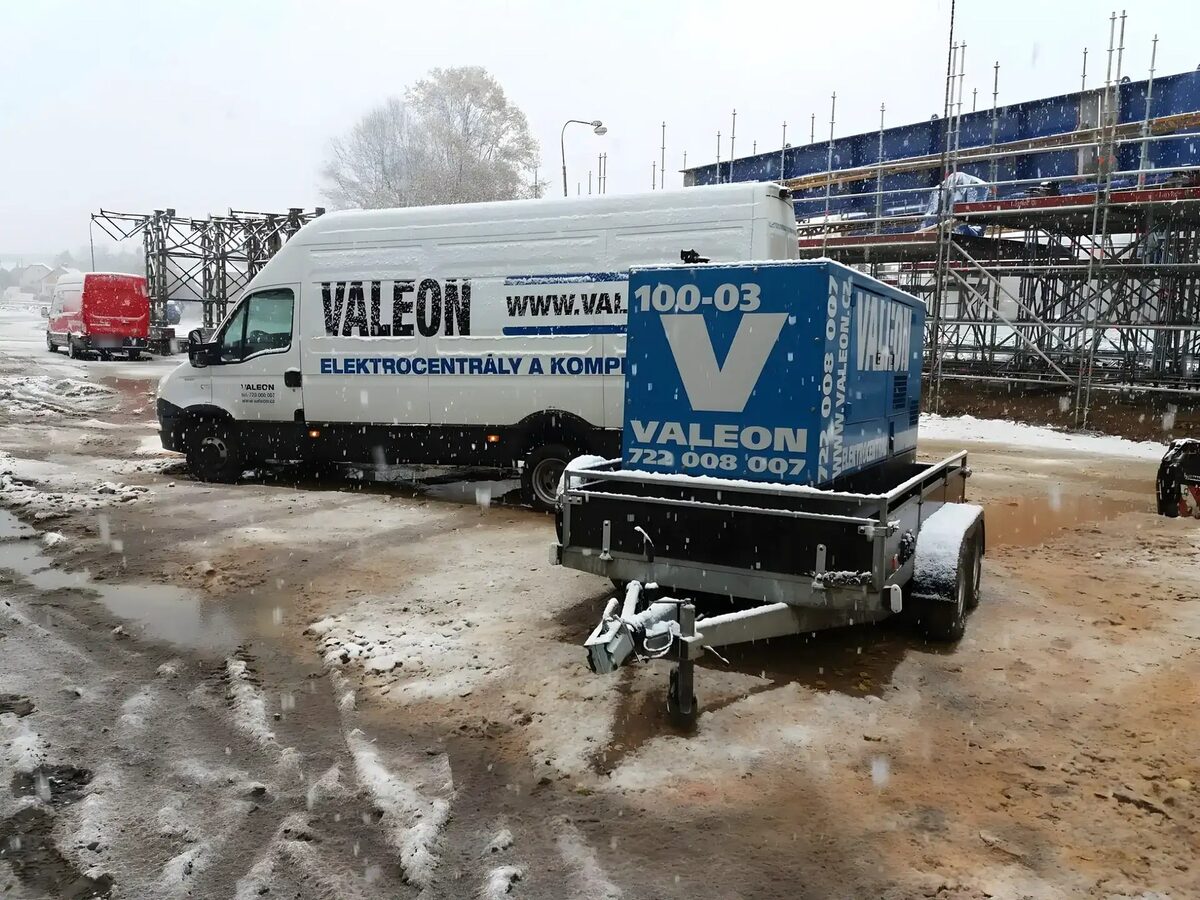 Elektrocentrála Valeon na přívěsu na zasněženém staveništi u ocelové konstrukce mostu na lešení