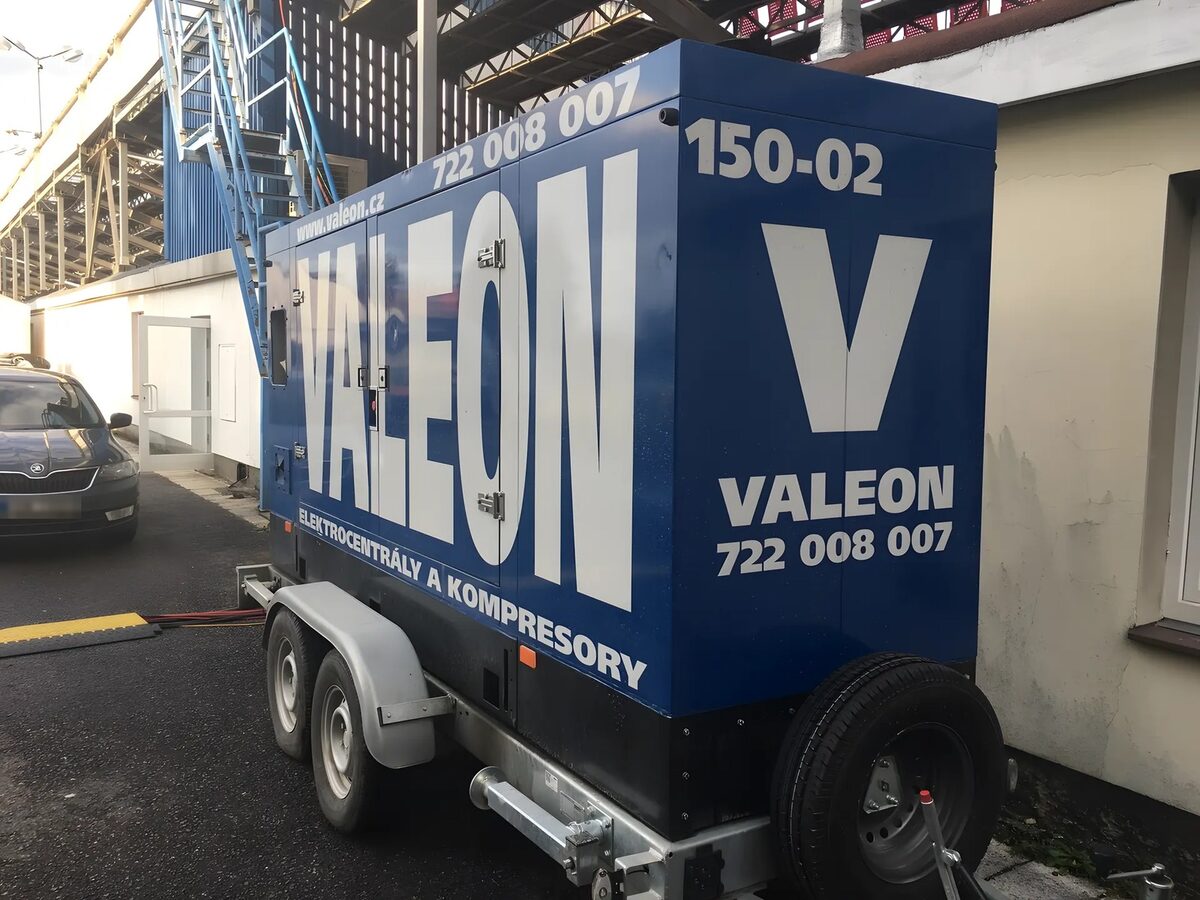 Elektrocentrála Valeon na přívěsu pod tribunou stadionu, kabely vedou přes kabelový přejezd